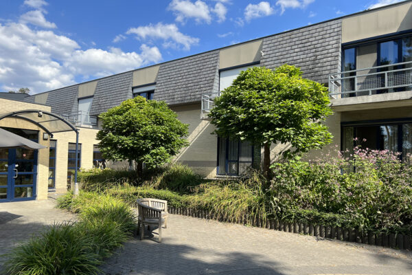 De assistentiewoningen van woonzorgcampus Beerzelhof, gezien vanaf de buitenkant. De ingang aan de linkerzijde is goed zichtbaar, waar grote blauwe dubbele deuren bezoekers verwelkomen.