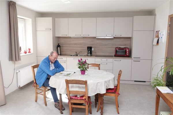 Ry du Chevreuil homme âgé qui lit un journal assis à une table dans une cuisine - Résidences-services - Eghezée